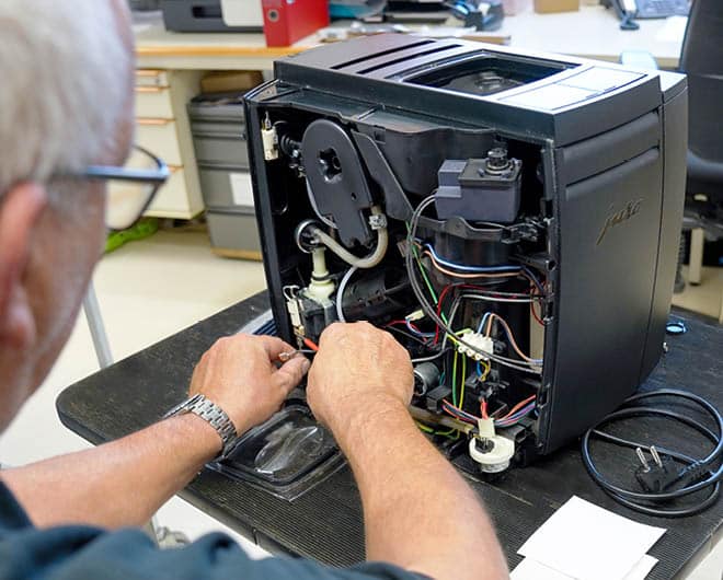 Fachmann repariert ein geöffnetes Jura-Kaffeegerät im ETECH Elektrofachhandel – Einblick in Elektronik und Verdrahtung