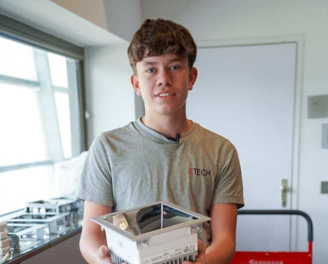 Junger ETECH-Mitarbeiter oder Lehrling hält ein Elektrobauteil in den Händen und trägt ein graues ETECH-T-Shirt.