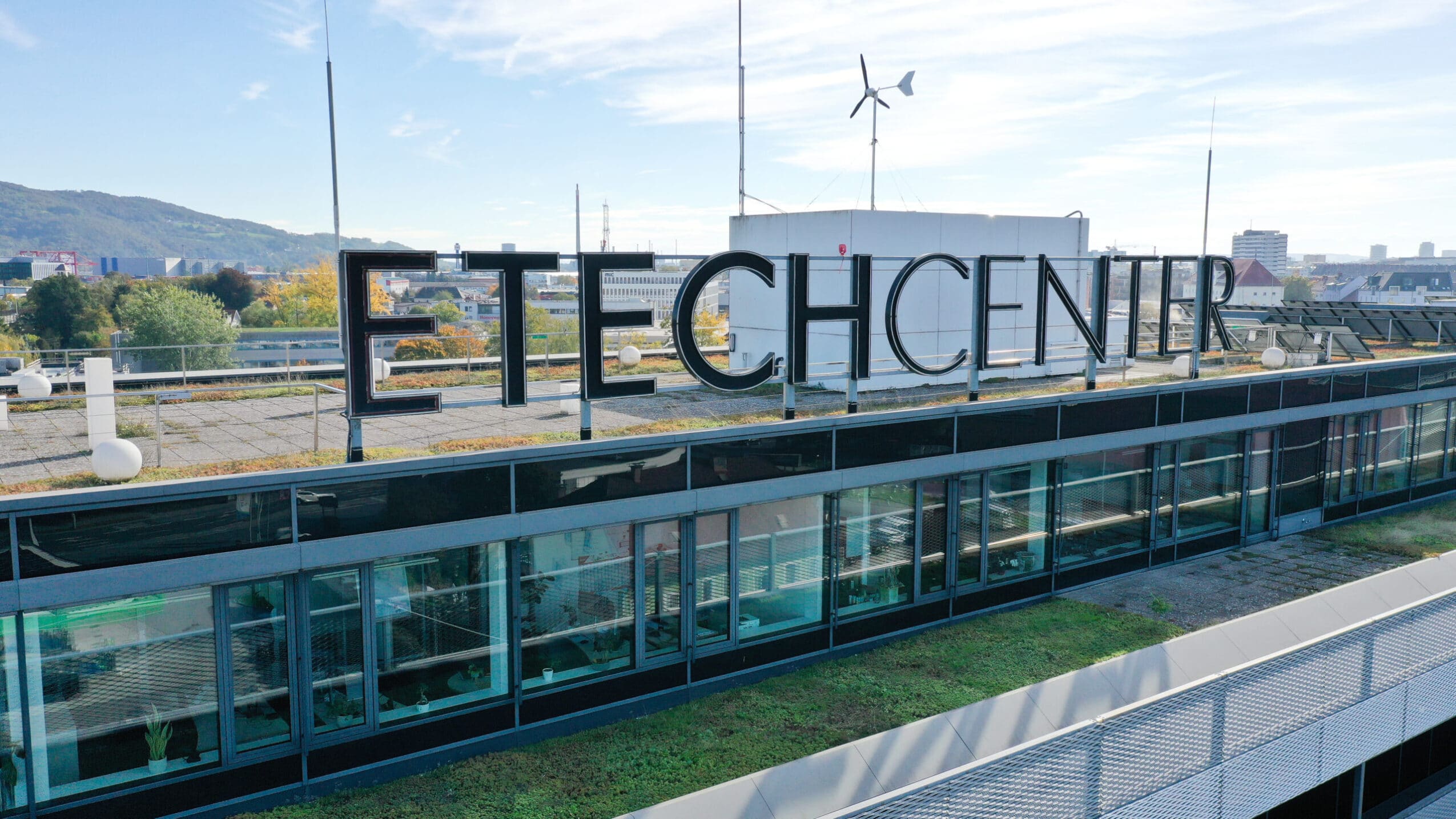 Dachaufschrift ETECHCENTER auf dem Gebäude des ETECH-Standorts in Linz mit Gründach, Solaranlagen und kleiner Windkraftanlage
