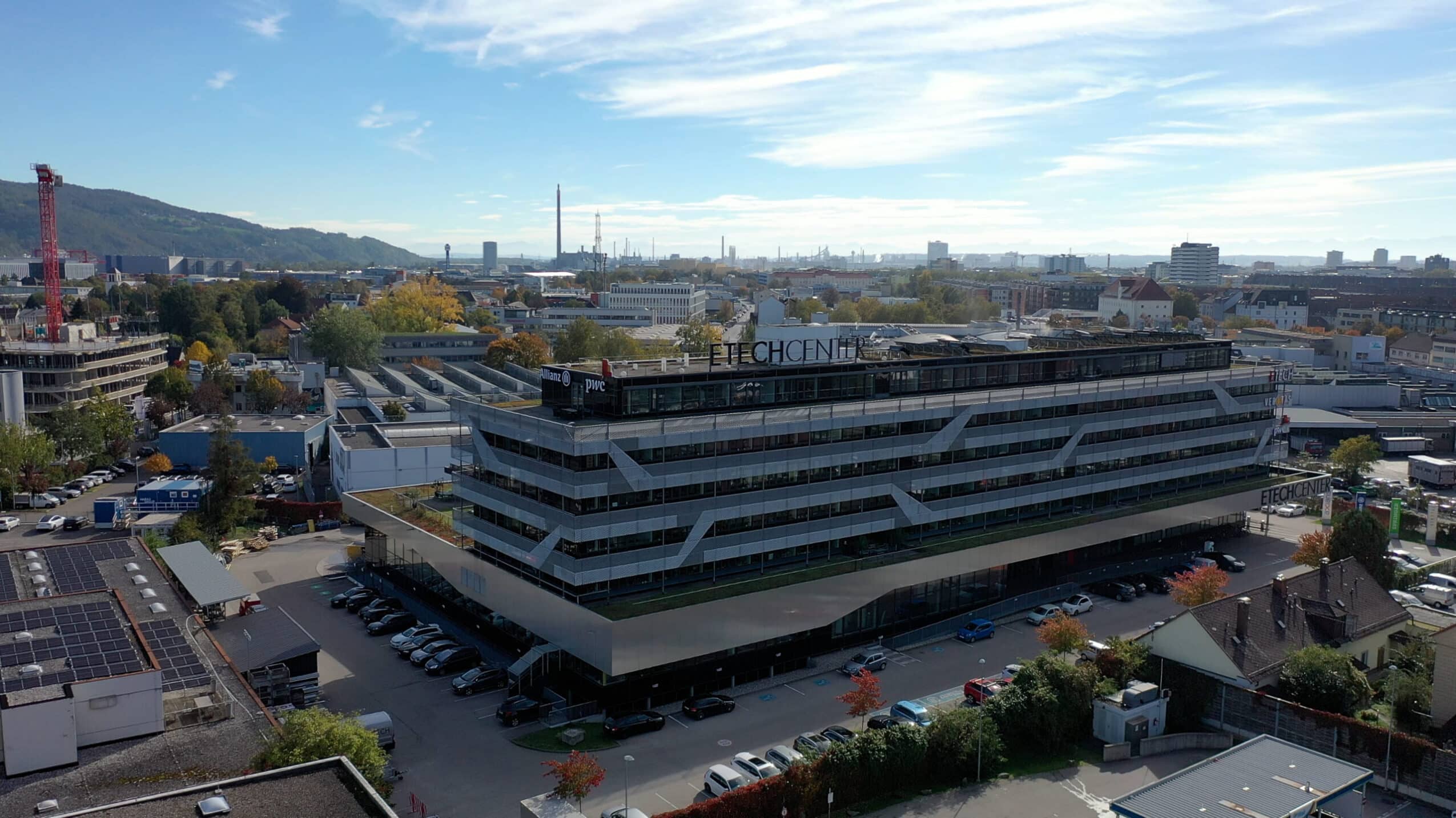 Luftaufnahme des ETECH Centers in Linz mit modernem Bürogebäude, Allianz- und PwC-Logos auf dem Dach, umgeben von Stadtpanorama