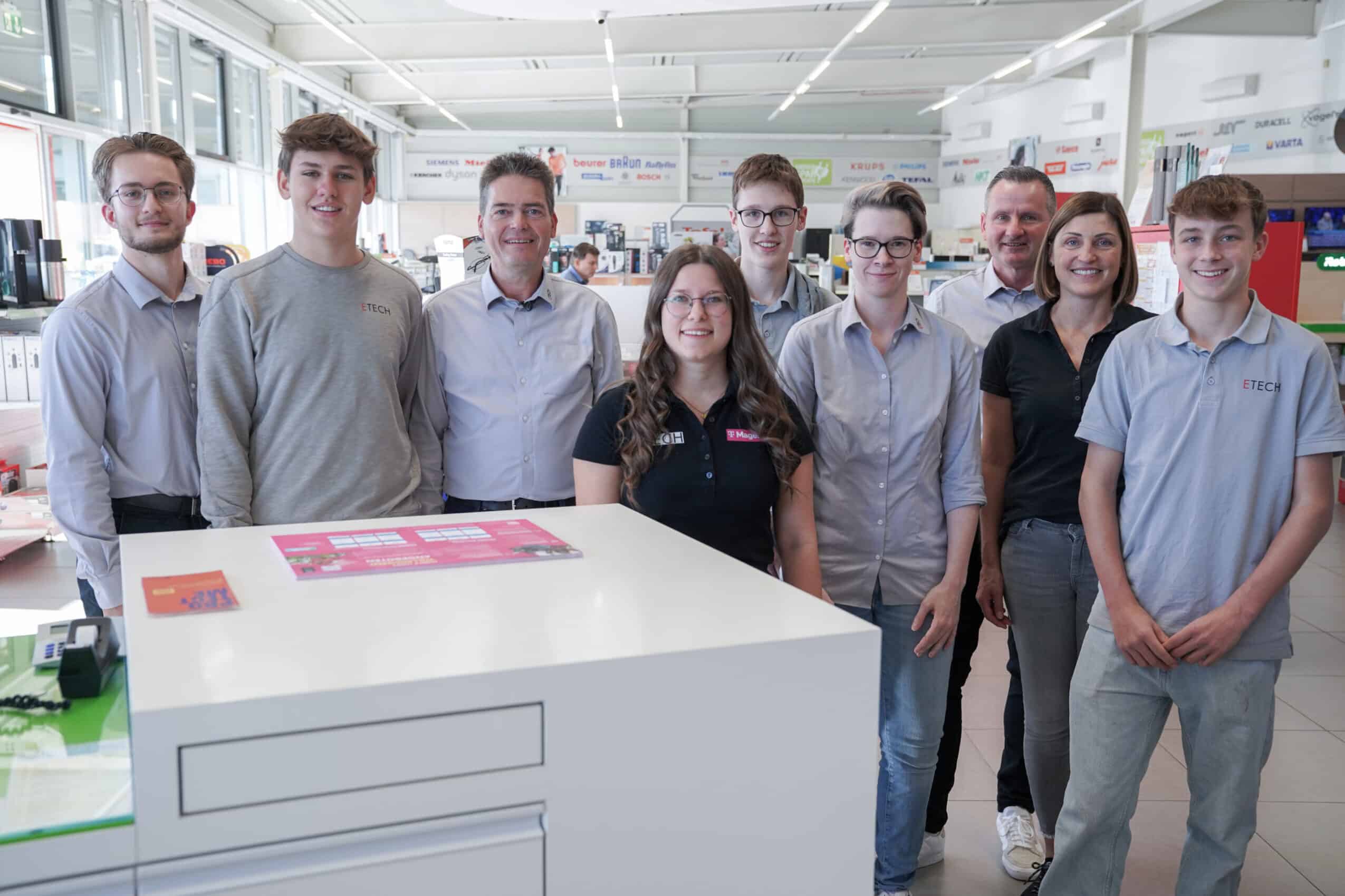 Team des ETECH-Standorts Rohrbach: neun Mitarbeiter und Lehrlinge posieren gemeinsam im Elektrofachhandel vor einem Verkaufstresen.