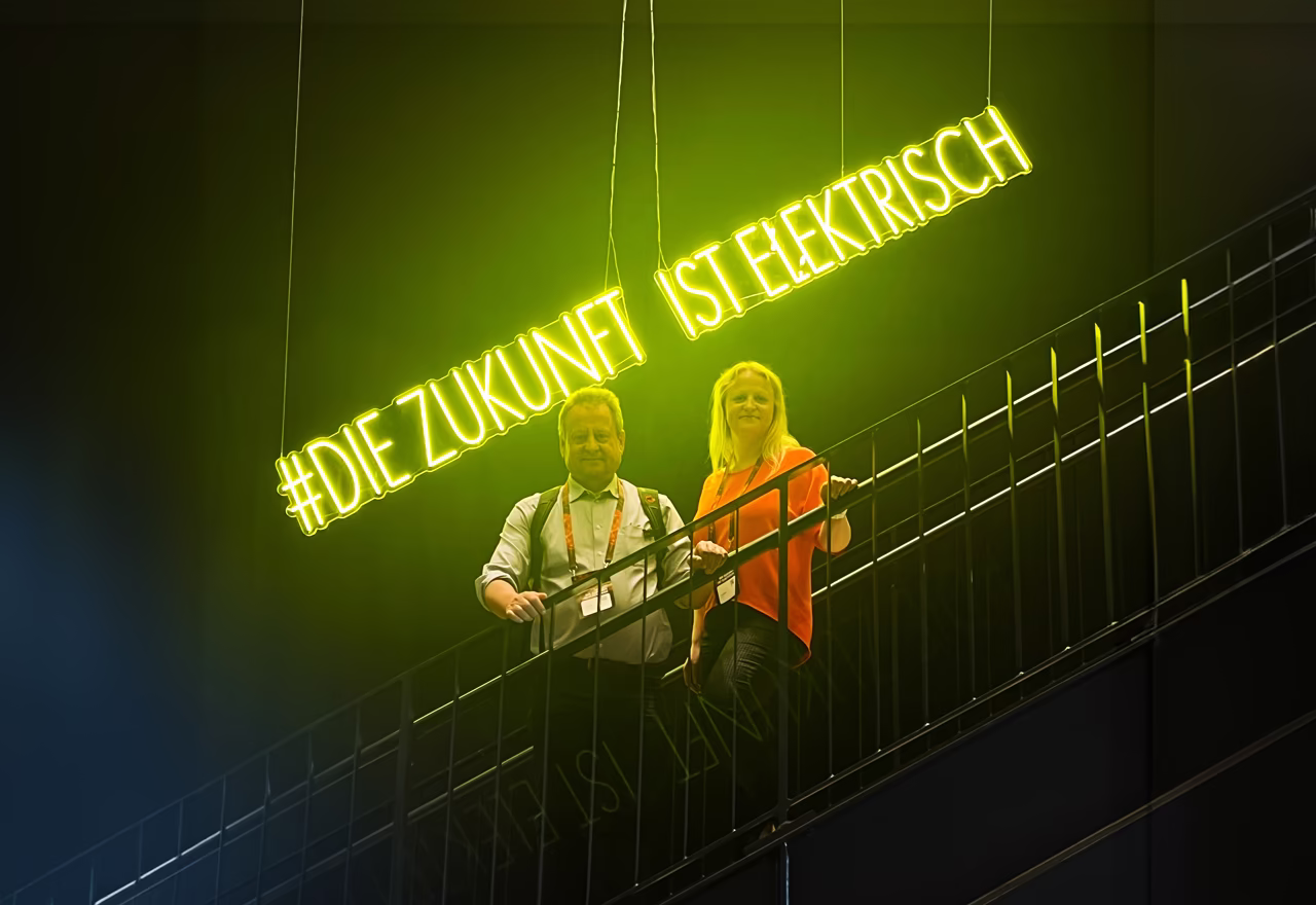 Zwei ETECH-Mitarbeiter auf einer Treppe unter einem leuchtenden Neonschild mit dem Hashtag #DieZukunftIstElektrisch