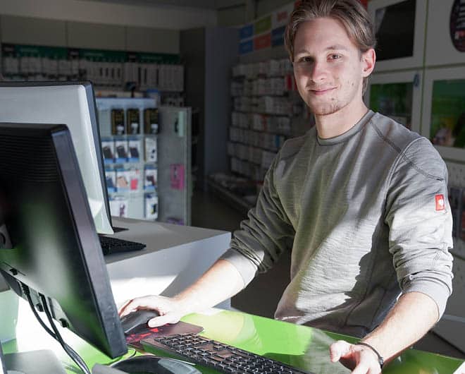 Junger ETECH-Mitarbeiter am Computer-Arbeitsplatz in einer Elektrofachhandel-Filiale