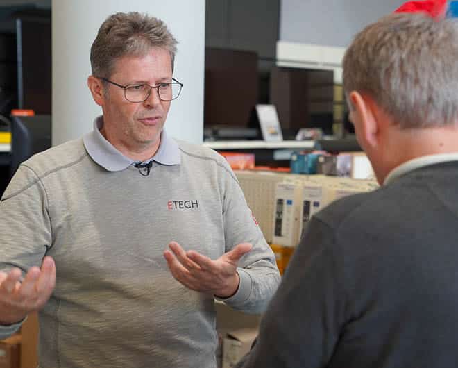 ETECH-Mitarbeiter im Gespräch mit einem Kunden im Elektrofachhandel, erklärt etwas mit Handgesten