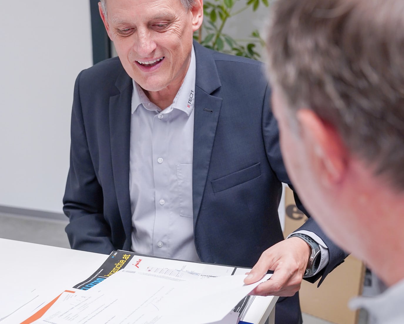 Zwei Männer im ETECH-Büro besprechen Dokumente und Unterlagen über den Elektrofachhandel – einer lächelt und zeigt auf Papiere.