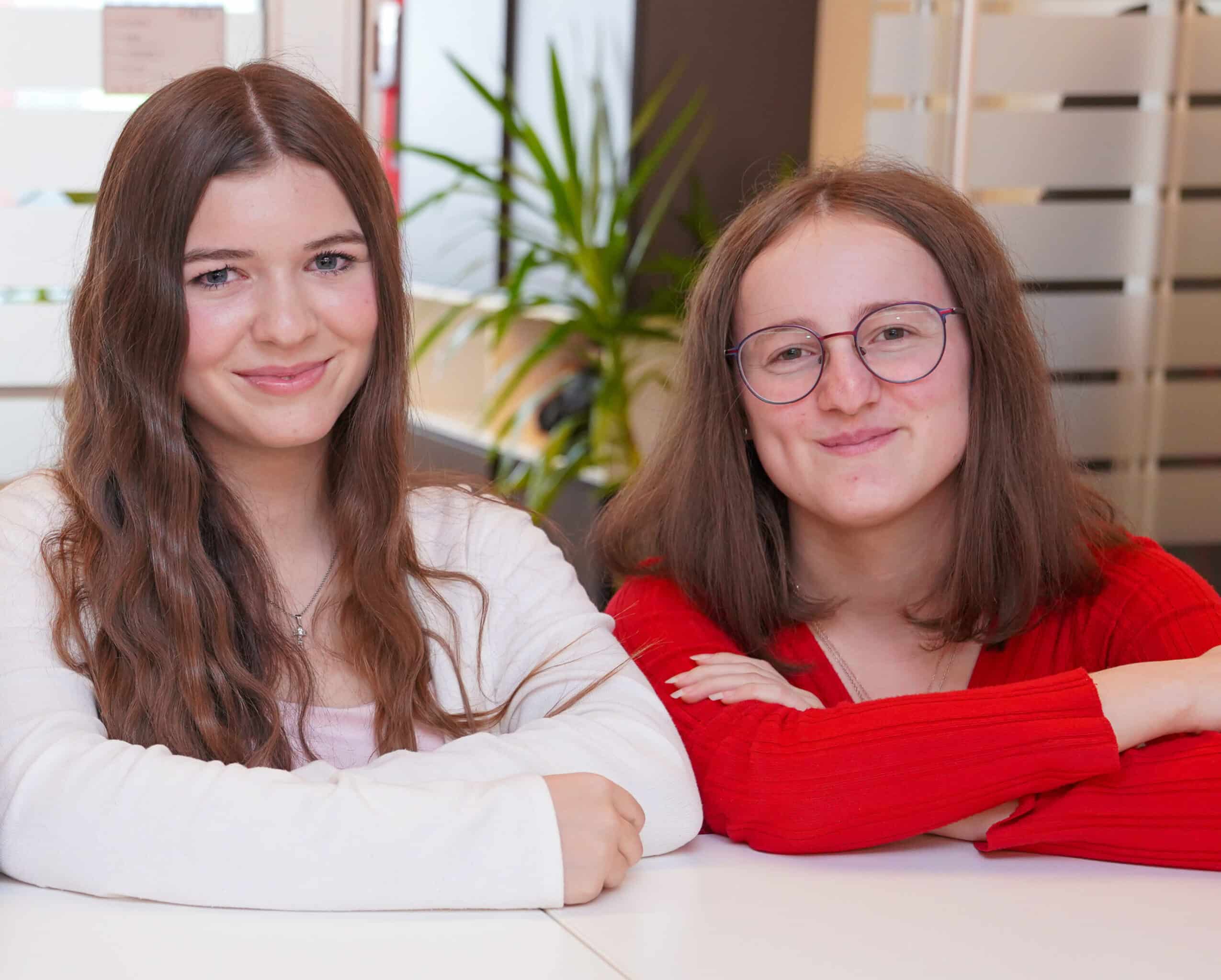 Zwei Lehrlinge bei ETECH sitzen lächelnd an einem Tisch im Büro.