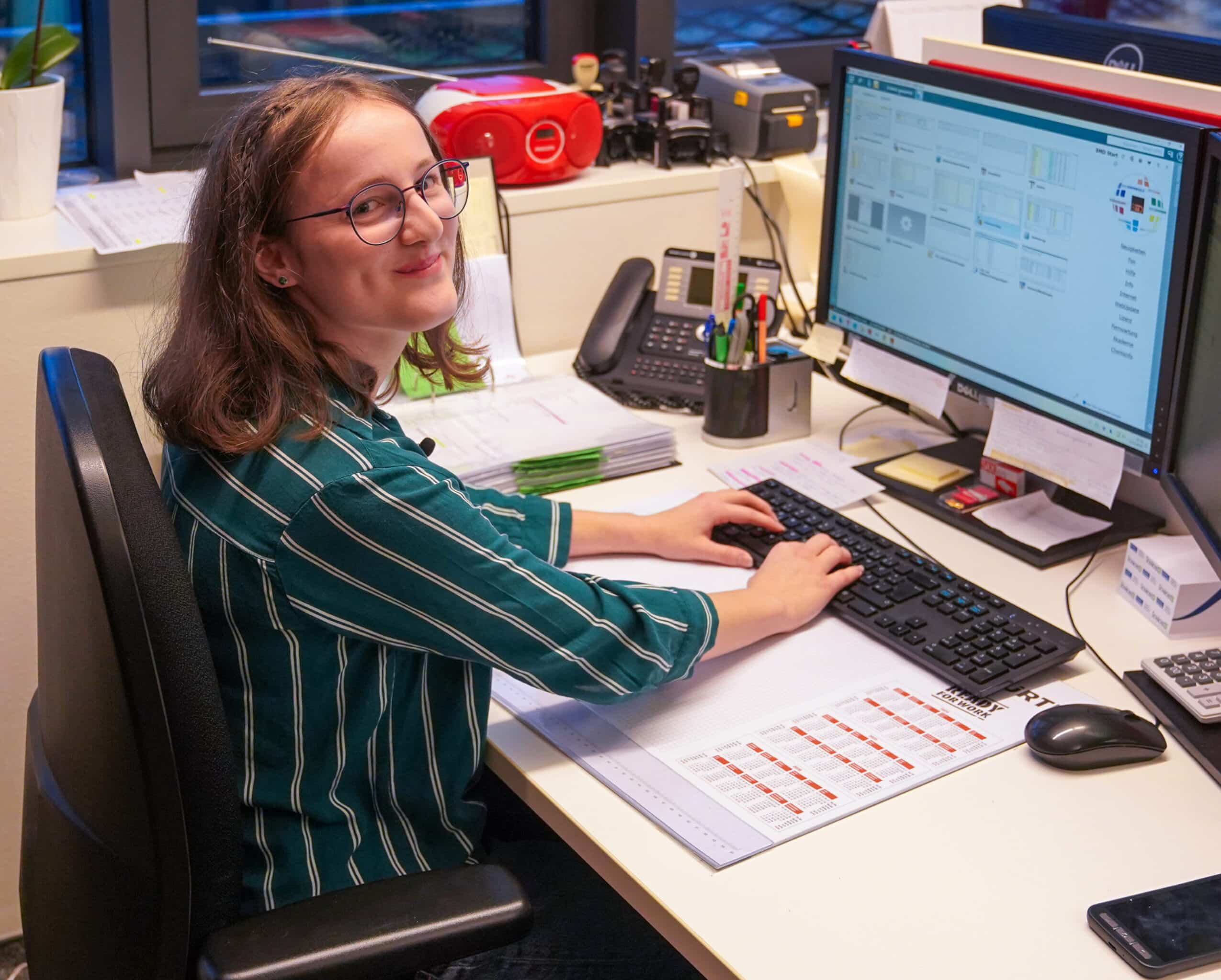 Lehrling bei ETECH Schmid u. Pachler Elektrotechnik arbeitet lächelnd an einem Dell-Computer in einem Büro.