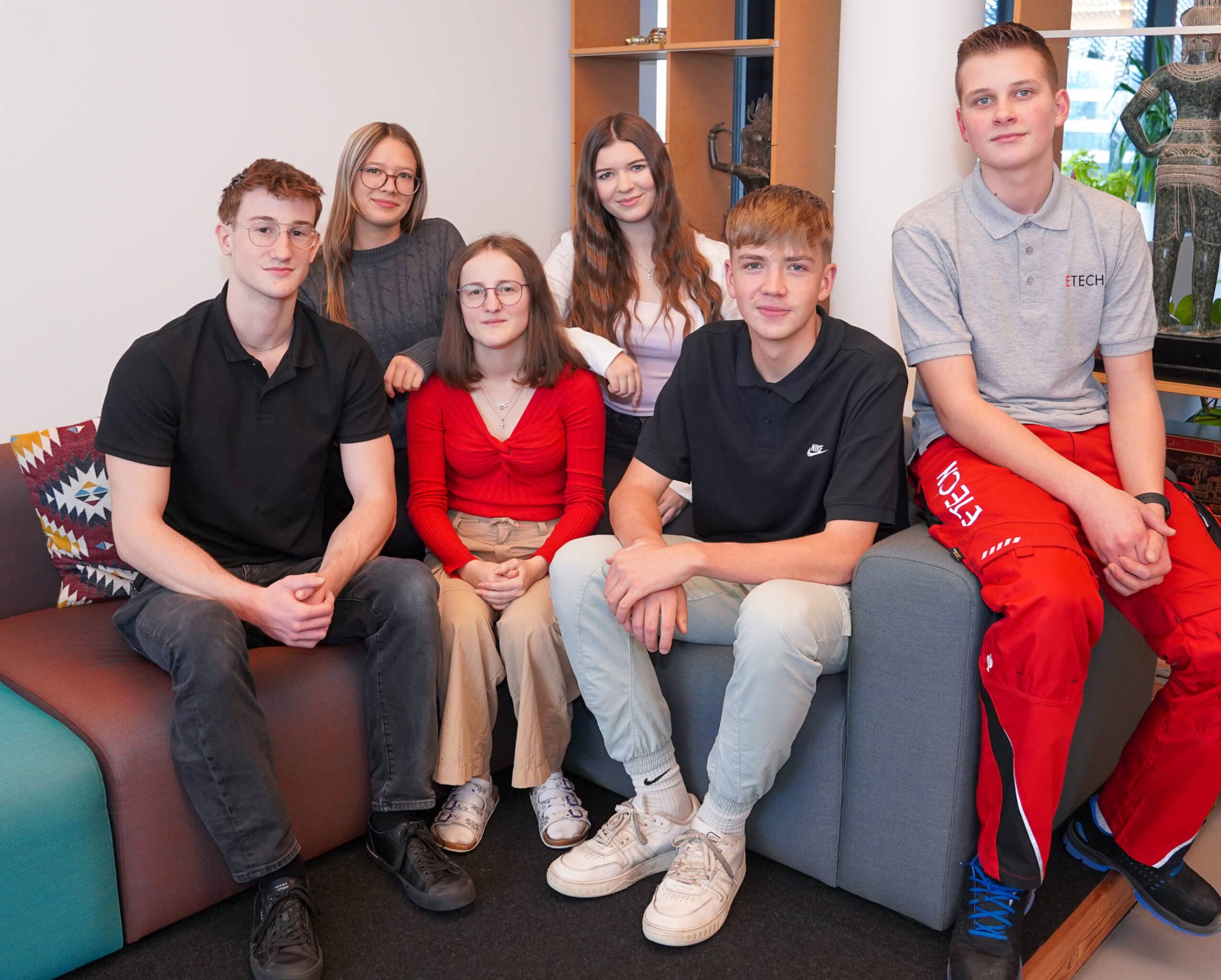 Sechs ETECH-Lehrlinge posieren gemeinsam auf einem Sofa in einem modernen Büro.