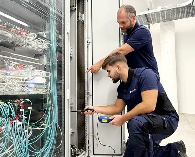 Zwei ETECH-Mitarbeiter arbeiten an einem Serverschrank mit Netzwerkkabeln in einem Rechenzentrum