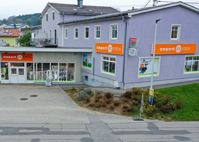 Expert ETECH Standort Grein – Außenansicht des Elektrofachhandels mit orangefarbenen Werbeschildern an einem lila Gebäude