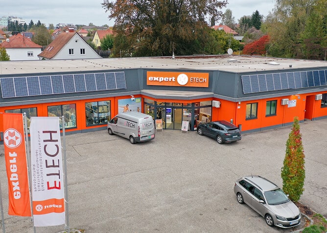 ETECH Schärding Filiale mit orangefarbener Fassade, Solaranlage auf dem Dach, Firmenfahrzeug und Flagge im Vordergrund