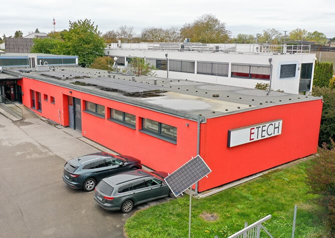 Luftaufnahme des ETECH-Standorts Wels: rotes Firmengebäude mit Solarpanelen auf dem Dach und im Außenbereich